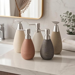 Puede incluir: Cinco dispensadores de jabón decorativos en varios colores, incluyendo beige, rosa, blanco y marrón. Cada dispensador tiene una bomba plateada y un cuerpo texturizado en forma de lágrima. Los dispensadores están colocados sobre una encimera blanca.