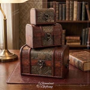 May include: Three stacked, antique-style wooden treasure chests. The chests are brown with ornate metal accents and clasps. The largest chest is at the bottom, with a medium and small chest stacked on top. The chests are on a wooden surface.