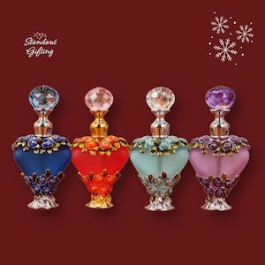 Peut inclure: Quatre flacons de parfum ornés, bleus, rouges, turquoise et violets, chacun avec un bouchon en cristal et des détails floraux. Les flacons ont une forme de cœur et sont posés sur un fond rouge foncé. Le texte indique "Standout Gifting".