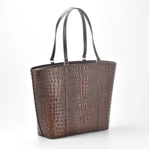May include: A brown leather tote bag with a crocodile-embossed pattern. The bag has two top handles and a spacious interior.