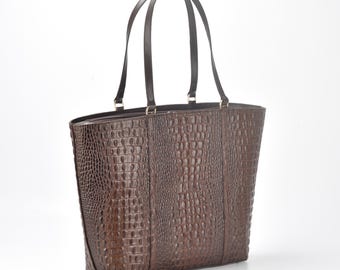 May include: A brown leather tote bag with a crocodile-embossed pattern. The bag has two top handles and a spacious interior.