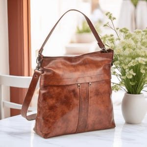 May include: A brown leather hobo bag with a long strap and a flap closure. The bag has a distressed look and is made of high-quality leather.