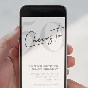 May include: A mobile phone screen shows a digital invitation for a 50th birthday celebration. The invitation reads "Cheers To" in cursive script above a large "50". The date, time, and location are also displayed on the screen.