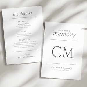 May include: Two white cards with black text. One card reads "the details" with event information. The other card says "In Loving Memory" with the initials "CM" and dates. The cards are on a white surface with shadows.
