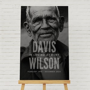 May include: A black and white memorial sign featuring a portrait of an older man. The sign reads "DAVIS IN LOVING MEMORY WILSON" with dates "FEBRUARY 1994 - DECEMBER 2024". The sign is displayed on a wooden easel.