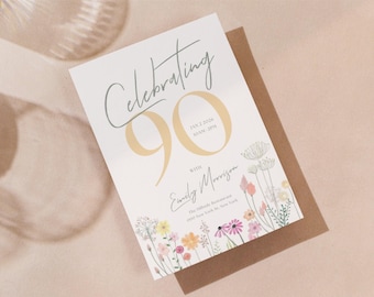 May include: A white card with a floral design and the text "Celebrating 90" in gold lettering. The card also includes the date "Jan 2, 2024" and the time "6:00 PM" in smaller text. The text "with Emily Morrison" is written in cursive below the number 90. The card is on a brown background.