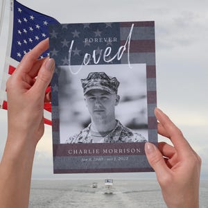 Könnte beinhalten: Eine Gedenkkarte mit einem Schwarz-Weiß-Porträt eines Mannes in Uniform, mit dem Schriftzug "Forever Loved" und dem Namen "Charlie Morrison" sowie Daten, vor einer amerikanischen Flagge.