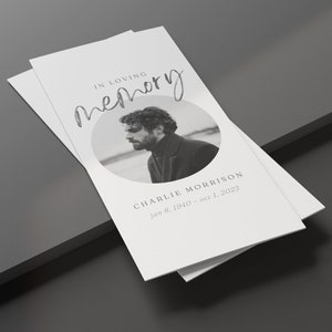 Puede incluir: Un montón de tarjetas conmemorativas con el texto "IN LOVING MEMORY" en escritura cursiva. Una foto en blanco y negro de un hombre está en un marco circular. El nombre "CHARLIE MORRISON" y las fechas están impresos debajo.