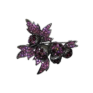May include: A silver-toned brooch featuring a cluster of stylized berries and leaves. The berries and leaves are encrusted with varying shades of purple rhinestones. The brooch has a pin closure on the back.