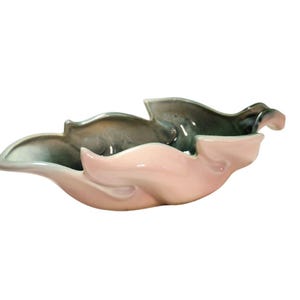 May include: A ceramic decorative bowl in a leaf shape. The bowl has a two-tone color scheme, with a light pink interior and a gray-green exterior. The bowl has a glossy finish and is likely vintage.