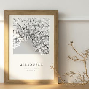 May include: A framed wall art print featuring a black and white street map of Melbourne, Australia. The map displays a grid of roads and a grey coastal area. Below the map, the text reads MELBOURNE, followed by coordinates and AUSTRALIA.