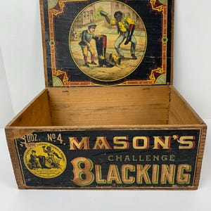 Puede incluir: Caja de madera vintage con una etiqueta negra y amarilla que dice "3 doz. No. 4 Mason's Challenge Blacking". La tapa de la caja tiene una ilustración colorida de tres personas, dos de las cuales son negras, en una escena de calle.