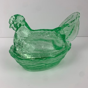 Op de afbeelding: Een groene glazen schaal in de vorm van een kip met een textuur. De kip zit in een nestachtige kom, met een gedetailleerde kop, lichaam en staartveren. Het item is decoratief.