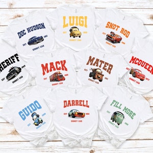 Peut inclure: Dix t-shirts blancs avec diff&eacute;rents personnages de Cars, le film de Disney Pixar. Chaque t-shirt pr&eacute;sente le nom d'un personnage diff&eacute;rent, une image de dessin anim&eacute; du personnage et le texte "EST" suivi de l'ann&eacute;e de cr&eacute;ation du personnage dans le film et "DISNEY CAR".