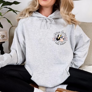 Op de afbeelding: Een lichtgrijze hoodie met een trekkoord. De hoodie heeft een cirkelvormige afbeelding met Mickey Mouse met een matrozenhoed, de woorden "Disney Cruise 2026" en "Mrs. Brown".