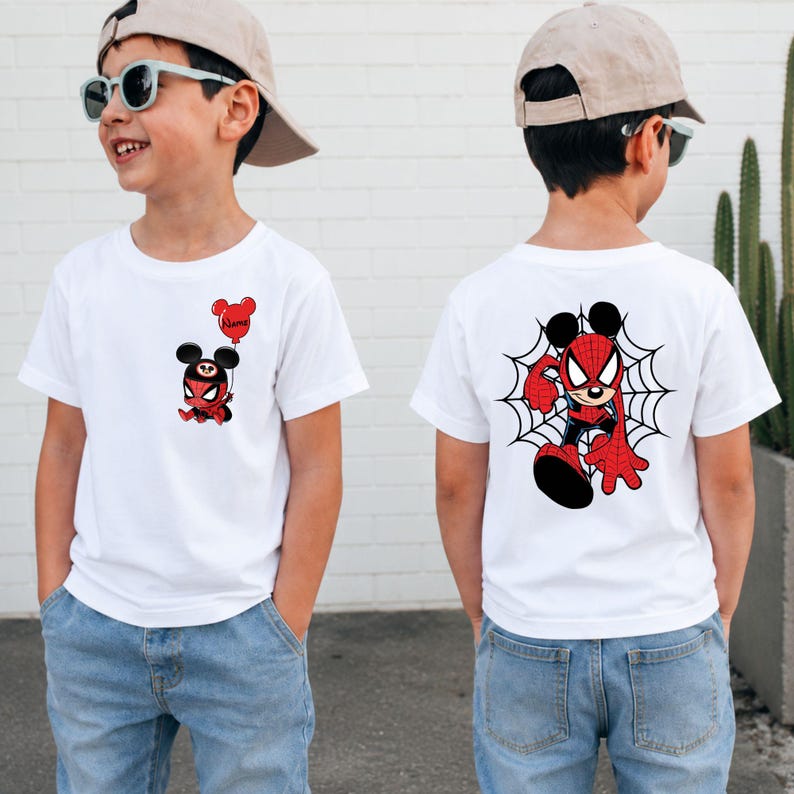May include: A white short-sleeved t-shirt featuring a small graphic on the front left chest of a character wearing a red and black spider-themed mask with mouse ears holding a red balloon, and a large graphic on the back of the same character.