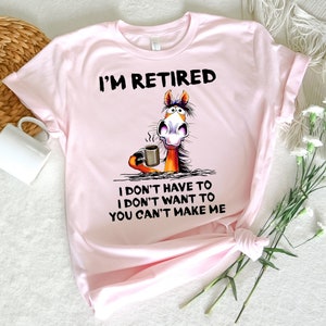 Pu&ograve; includere: Maglietta rosa con un cavallo dei cartoni animati che tiene una tazza di caff&egrave;. Il testo sulla maglietta recita "I'm Retired I don't have to I don't want to You can't make me."