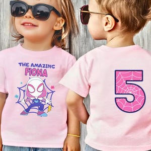 May include: Two pink t-shirts. One features the text "THE AMAZING FIONA" and a cartoon character. The other has a large number 5 with a spiderweb design. Both shirts are short-sleeved.