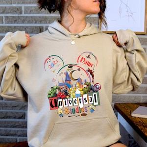 May include: A tan hoodie with a graphic of a Mickey Mouse head featuring characters from popular movies and TV shows, including Harry Potter, The Simpsons, and Marvel superheroes. The text "Universal Studios" is printed below the graphic.