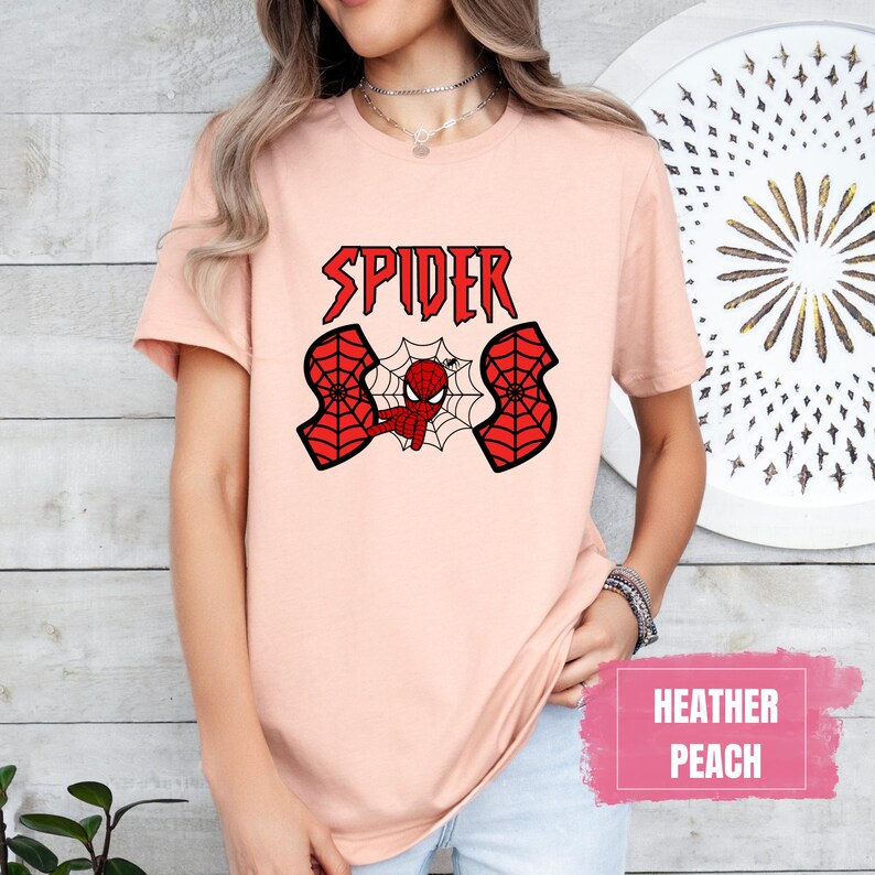 May include: A peach colored t-shirt with a red spider-man graphic and the text "SPIDER" in black letters. The shirt is made of a soft, comfortable material.