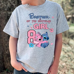 以下が含まれることがあります： 青とピンクで「Brother of the Birthday Girl」と書かれたグレーのTシャツ。数字の8はピンク色で、漫画のキャラクターが抱き合っています。ピンクと青の花と星のアクセントがデザインを完成させています。