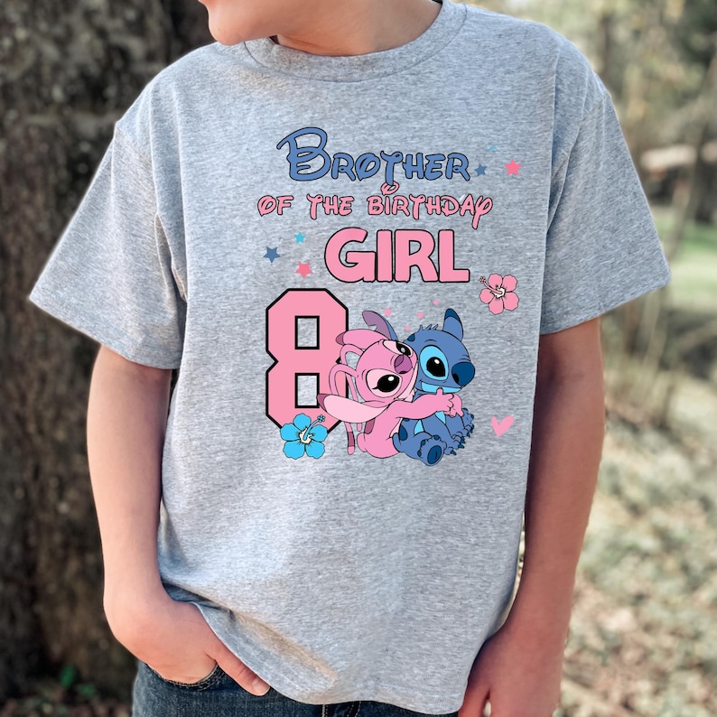 以下が含まれることがあります： 青とピンクで「Brother of the Birthday Girl」と書かれたグレーのTシャツ。数字の8はピンク色で、漫画のキャラクターが抱き合っています。ピンクと青の花と星のアクセントがデザインを完成させています。