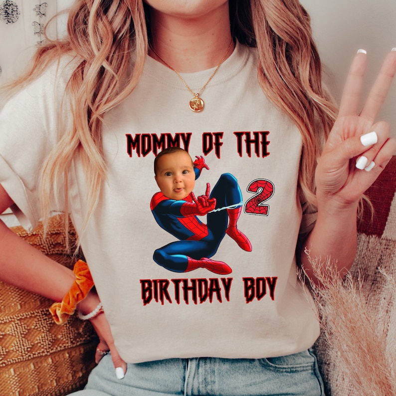 Puede incluir: Una camiseta blanca con el texto "Mommy of the 2 Birthday Boy" en rojo. Una imagen de dibujos animados de Spiderman con la cara de un beb&eacute; superpuesta sobre su cabeza est&aacute; en el centro de la camiseta.