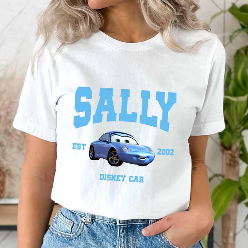 Peut inclure: T-shirt blanc avec un graphique bleu de Sally de Cars de Disney. Le graphique comprend le texte "Sally", "EST 2002" et "Disney Car".