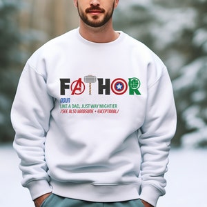 May include: White sweatshirt with a graphic design that says "FATHOR" with superhero logos incorporated into the letters. The text below says "NOUN LIKE A DAD, JUST WAY MIGHTIER /SEE ALSO HANDSOME + EXCEPTIONAL/"