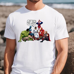 Puede incluir: Camiseta blanca con una ilustraci&oacute;n de estilo c&oacute;mic de superh&eacute;roes y Jes&uacute;s. La imagen incluye a Hulk, Capit&aacute;n Am&eacute;rica, Iron Man, Thor y Spider-Man. El texto en un bocadillo dice: "...&iexcl;Y AS&Iacute; ES COMO SALV&Eacute; EL MUNDO!"