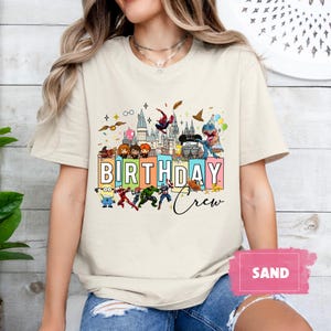 May include: A white t-shirt with a colorful graphic of cartoon characters, including a minion, Spiderman, and characters from Harry Potter. The graphic includes the text "Birthday Crew".