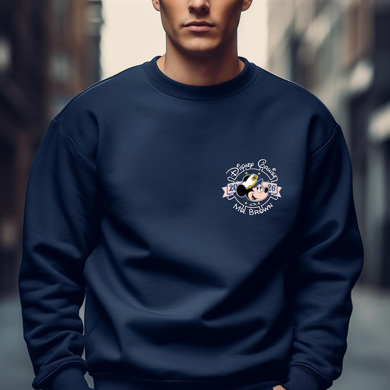 Op de afbeelding: Marineblauw sweatshirt met een kleine afbeelding op de borst. De afbeelding bevat de tekst "Disney Cruise", een Mickey Mouse-afbeelding, de cijfers "20" en "26" en de naam "Mr. Brown". Het ontwerp staat in een cirkelvormig embleem.