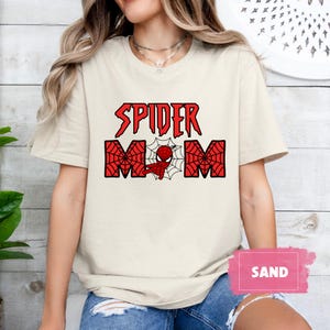 May include: A white t-shirt with a red and black graphic that says "Spider Mom" with a cartoon image of Spiderman in the middle of the word "Mom".