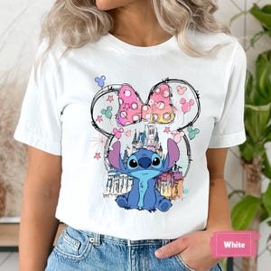 May include: White t-shirt featuring a colorful graphic of the character Stitch from Lilo & Stitch, with a pink polka-dot bow and a castle. The design is surrounded by stars and Mickey Mouse silhouettes.