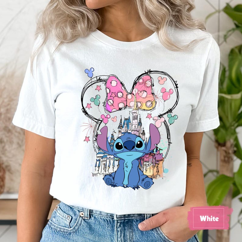 May include: White t-shirt featuring a colorful graphic of the character Stitch from Lilo & Stitch, with a pink polka-dot bow and a castle. The design is surrounded by stars and Mickey Mouse silhouettes.