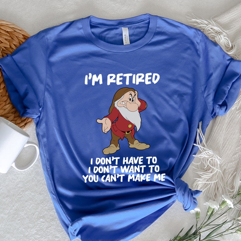 May include: A blue t-shirt with a white graphic of a cartoon dwarf with a white beard and red clothing. The text "I'm Retired I don't have to I don't want to You can't make me" is printed in white on the shirt.