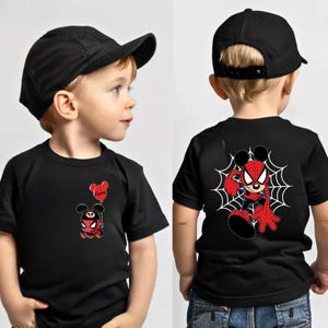 May include: A black t-shirt featuring a small graphic of a character with mouse ears and a spider-themed suit holding a red balloon on the front, and a larger graphic of the same character on a spider web on the back, paired with a black cap.