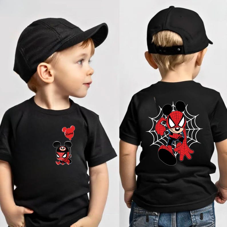 May include: A black t-shirt featuring a small graphic of a character with mouse ears and a spider-themed suit holding a red balloon on the front, and a larger graphic of the same character on a spider web on the back, paired with a black cap.