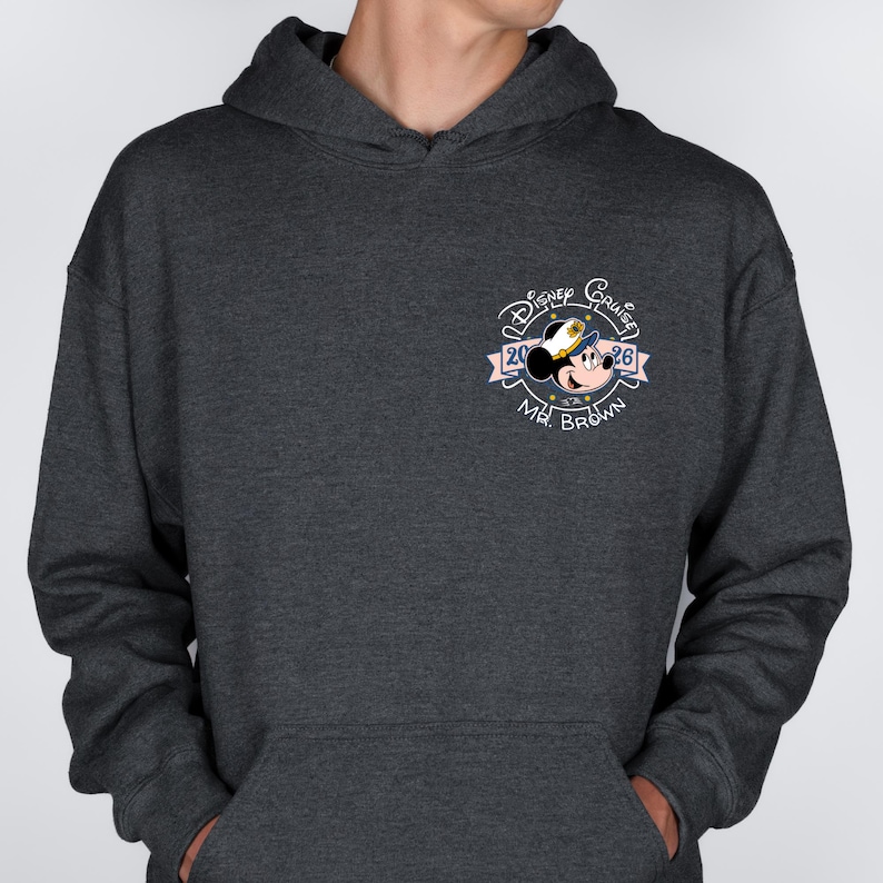 Op de afbeelding: Donkergrijze hoodie met een Disney Cruise-ontwerp. Het ontwerp bevat Mickey Mouse met een kapiteinshoed, de woorden "Disney Cruise" en "2026", en de naam "Mr. Brown". De hoodie heeft een voorzak en een capuchon met trekkoord.