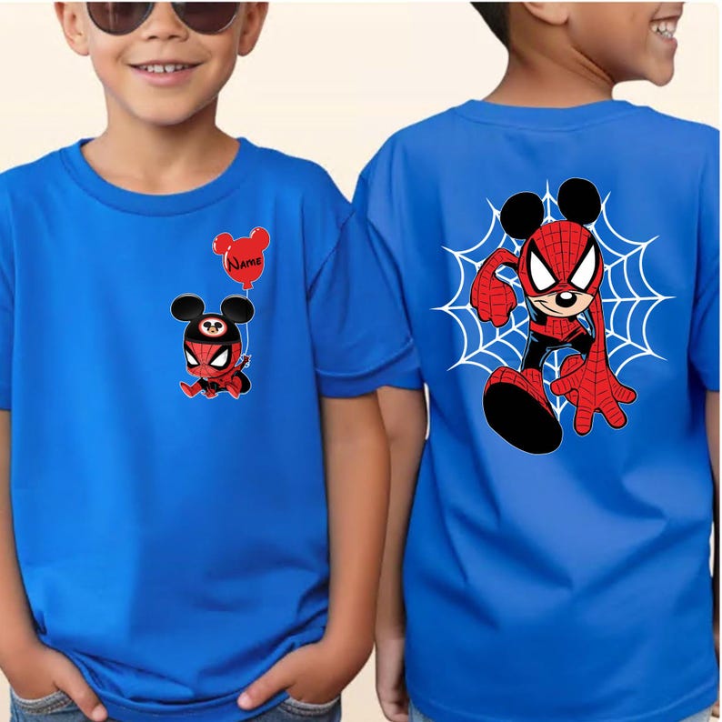 May include: A bright blue t-shirt featuring a small graphic on the front left chest of a character wearing a spider-themed mask and holding a red balloon with the text Name, and a large graphic on the back of the same character in a web design.