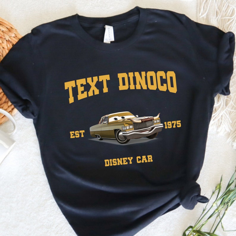 Peut inclure: T-shirt noir avec un graphique jaune d'une voiture vintage avec le texte "Text Dinoco Est 1975 Disney Car"