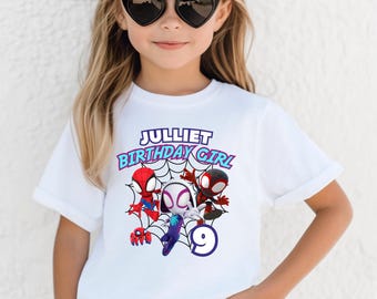 Op de afbeelding: Wit T-shirt met een kleurrijke afbeelding van Spider-Man-personages en de tekst "Julliet Birthday Girl" met het nummer 9. Het ontwerp bevat rode, zwarte en witte Spiderman-figuren op een web.