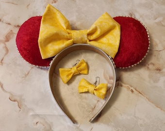 May include: A pair of red and yellow Minnie Mouse ears with a white headband. The ears are covered in a yellow fabric with a white swirl pattern. The headband is decorated with rhinestones. The ears are also adorned with a pair of yellow bow earrings.