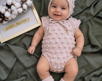 Conjunto de roupa de bebê para bebê, composto por body, touca e sapatinhos, tricotados à mão em bege com pompons.
