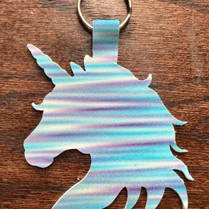 Könnte beinhalten: Ein blauer und lilafarbener, schimmernder Glitzer-Einhorn-Schlüsselanhänger mit einem silbernen Schlüsselring.