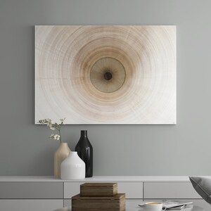 May include: A living room interior with a gray armchair, a coffee table with a black metal base, and a white wall with a circular abstract painting. The coffee table has a stack of wooden boxes and a cup of coffee on it.