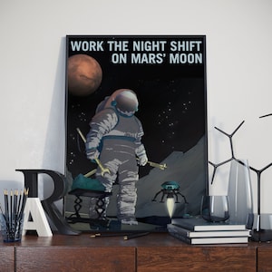 May include: A retro-style poster with a black background and white text that reads "Work the night shift on Mars' moon". The poster features an astronaut in a white spacesuit standing on a gray, rocky surface. A red planet is visible in the upper left corner of the poster. A small, blue, spider-like robot is in the foreground.