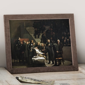 Può includere: Una stampa incorniciata di un dipinto del 1875 raffigurante una dimostrazione chirurgica. L'opera mostra un gruppo di uomini in abiti scuri riuniti attorno a un paziente, con un pubblico seduto che osserva. La cornice è di colore marrone scuro.