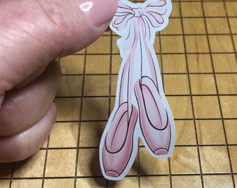 May include: Pink ballet shoes with a pink bow tied at the top. The shoes are on a white background.