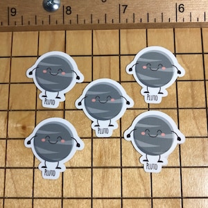 Peut inclure: Cinq autocollants Pluton souriants avec des bras. Chaque autocollant porte le mot "PLUTO" imprimé en bas. Les autocollants sont gris avec des rayures blanches et des joues roses. Une vis et une règle sont en arrière-plan.